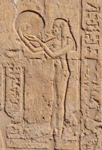 An engraved stone frieze that shows a woman playing a large round drum.